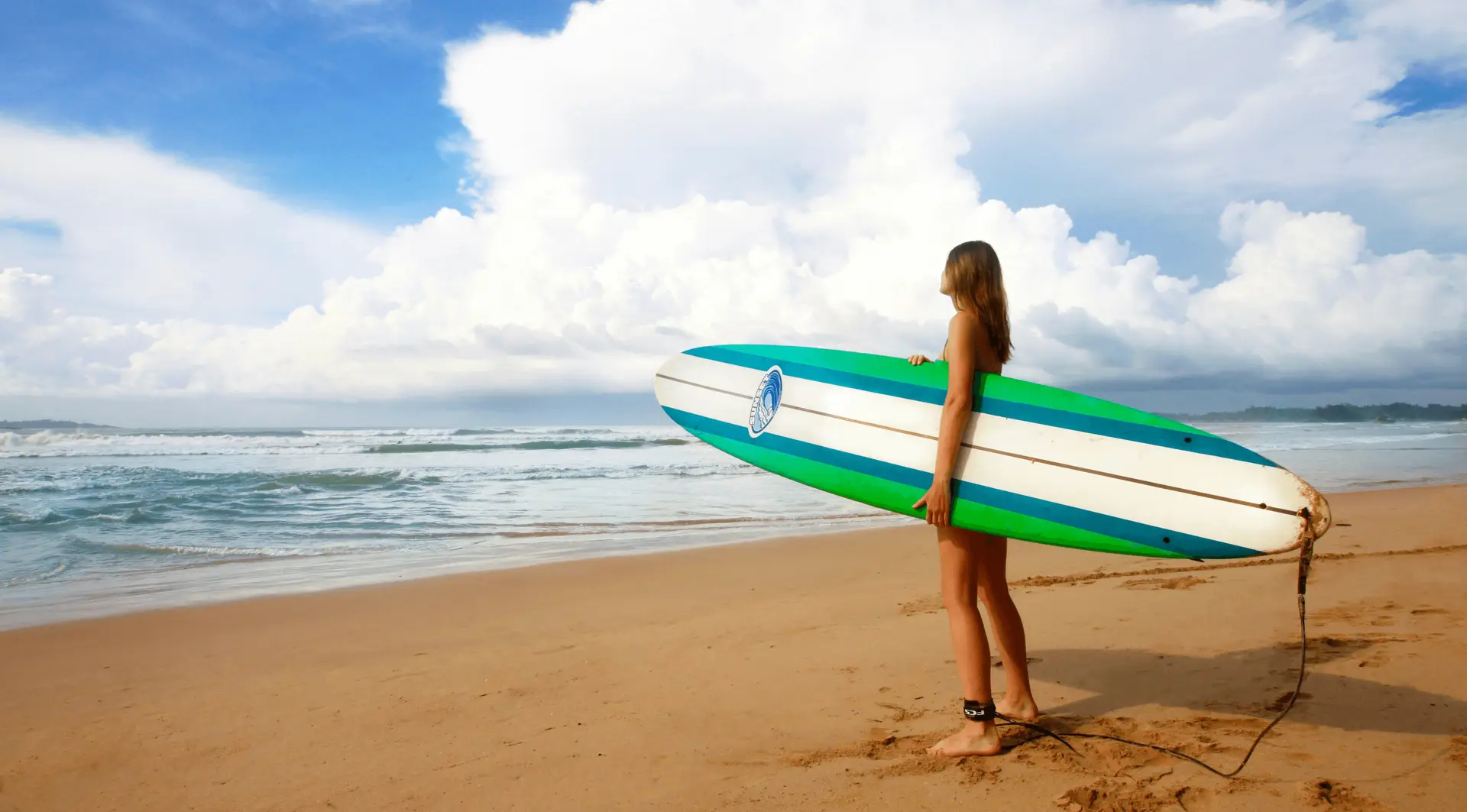 A surfer carrying a longboard on the sand at Mirissa beach